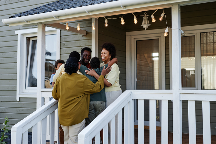 Portrait of happy black family embracing while standing on porch of new house, copy space